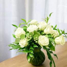White roses arranged in a green glass vase with lush foliage
