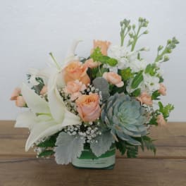 Peach roses and white lilies in a glass vase with a succulent