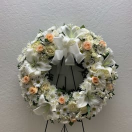 White floral wreath with peach roses and lilies on a stand