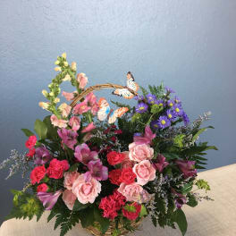 Basket arrangement of pink and purple flowers with butterfly picks