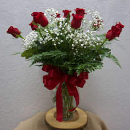 Red roses and white baby's breath in a glass vase with a red ribbon