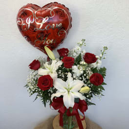 Red heart balloon above a bouquet of red roses and white lilies in a glass vase