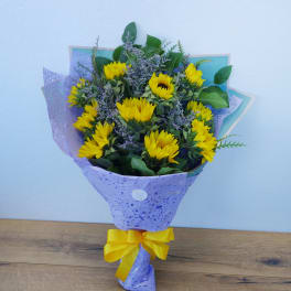 Bouquet of yellow sunflowers wrapped in purple paper with a yellow ribbon