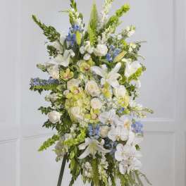 Tall white and green floral standing spray with blue accents on an easel