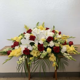 Large floral spray with red roses, white lilies, and yellow flowers on a stand