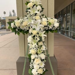 White floral cross on a stand with roses, lilies, and daisies