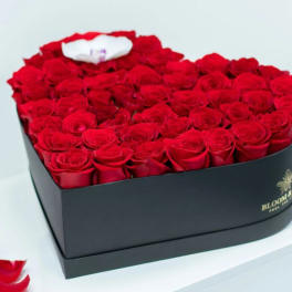 Heart-shaped box filled with red roses and a white accent flower