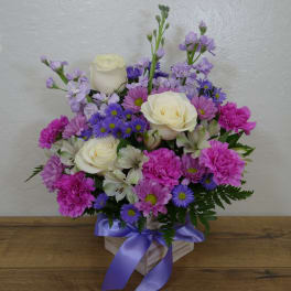Mixed bouquet of white roses, pink carnations, and purple daisies in a ribboned box