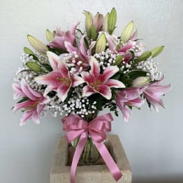Pink lilies in a glass vase with a pink ribbon bow