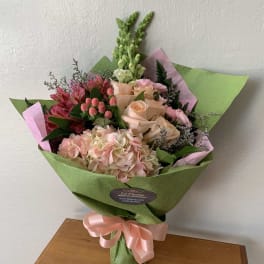 Bouquet of pink and peach flowers wrapped in green paper with a pink ribbon