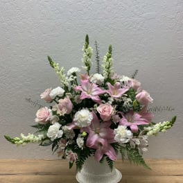 Pink lilies and roses arranged in a white vase with white filler flowers