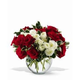 Round arrangement of red and white roses in a clear glass bowl vase with variegated foliage