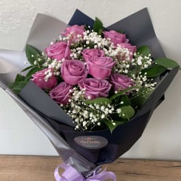 Bouquet of pink roses with white baby's breath in dark wrapping