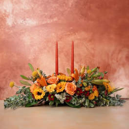 Low floral centerpiece with orange and yellow flowers and two red taper candles