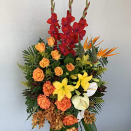 Tall tropical flower arrangement with red gladiolus, orange roses, yellow lilies, and white anthuriums