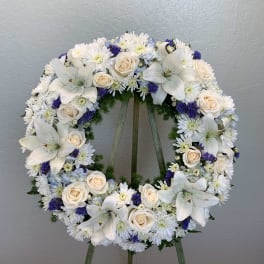 Circular floral wreath with white lilies, cream roses, and white daisies on an easel