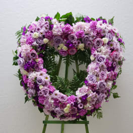 Heart-shaped floral wreath of pink and lavender flowers on a stand