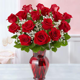 Red roses arranged in a red glass vase with white baby's breath