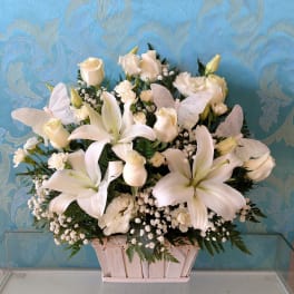 White lilies and roses arranged in a wooden basket with butterfly accents