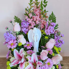 Pink and purple floral arrangement with lilies and roses around a white angel figurine