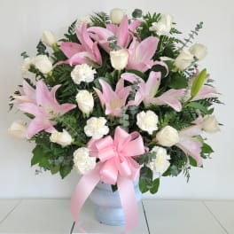 Pink lilies and white roses in a white vase with a pink ribbon