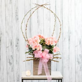 Pink flower arrangement in a rustic wooden box with tall twig arches and a sheer pink bow.
