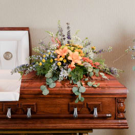 Floral spray on a wooden casket with peach lilies and mixed blooms