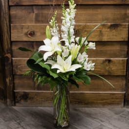 White lilies and snapdragons in a tall glass vase