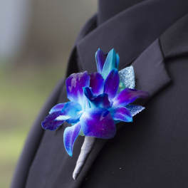 Blue and purple orchid boutonniere with glitter accents pinned to a black lapel