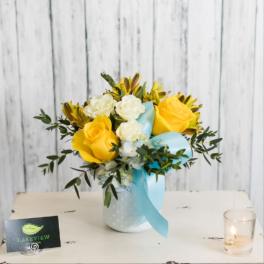 Yellow and white rose bouquet in a white vase with a blue ribbon