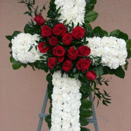 Cross-shaped floral tribute with red roses and white flowers on an easel