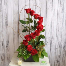 Tall arrangement of red roses in a black container with a candle nearby