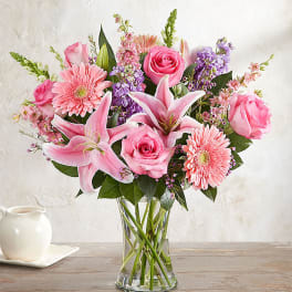 Pink roses, lilies, and gerbera daisies in a clear glass vase