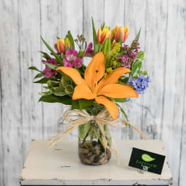 Mixed bouquet with orange lily and colorful tulips in a glass vase
