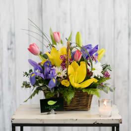 Basket arrangement of tulips, irises, and daisies with a candle beside it