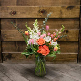 Mixed bouquet of pink, white, and orange flowers in a glass jar vase