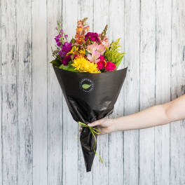 Handheld bouquet of mixed bright flowers wrapped in black paper
