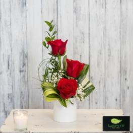 Red roses arranged in a white vase with baby's breath and greenery