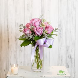 Pink roses in a clear glass vase with a lavender ribbon and candle