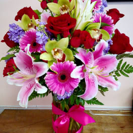 Bouquet of pink lilies, red roses, and purple flowers in a glass vase