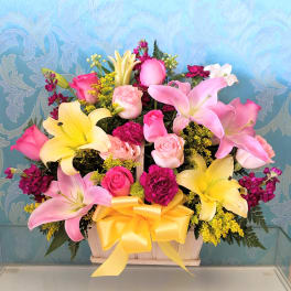 Pink and yellow lilies with roses in a wooden basket tied with a yellow bow