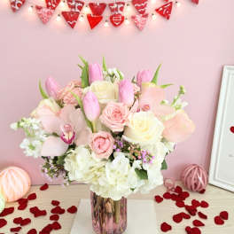Pink and white bouquet in a glass vase with rose petals around it
