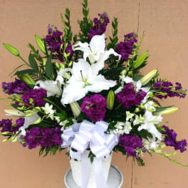 White lilies and purple flowers arranged in a white vase with a bow.