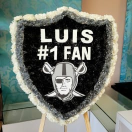 Heart-shaped floral tribute with black, white, and silver flowers and a sports logo