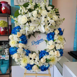 Large floral wreath with white lilies, roses, and blue hydrangeas around a Dodgers logo