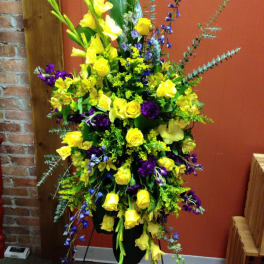Tall floral arrangement with yellow roses and purple flowers in a black stand