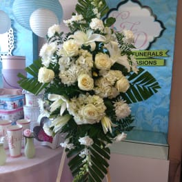 White floral standing spray on an easel with lilies and roses