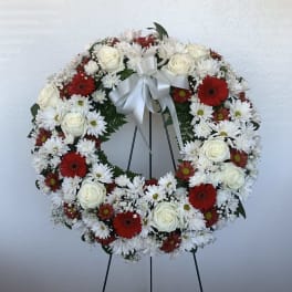 Circular wreath of white and red flowers on a stand with a white ribbon