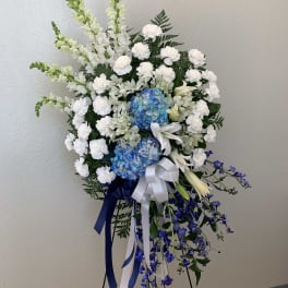 Standing floral spray with white and blue flowers on a black easel