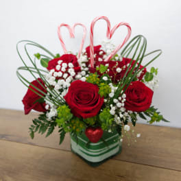 Red roses in a striped glass vase with candy cane hearts